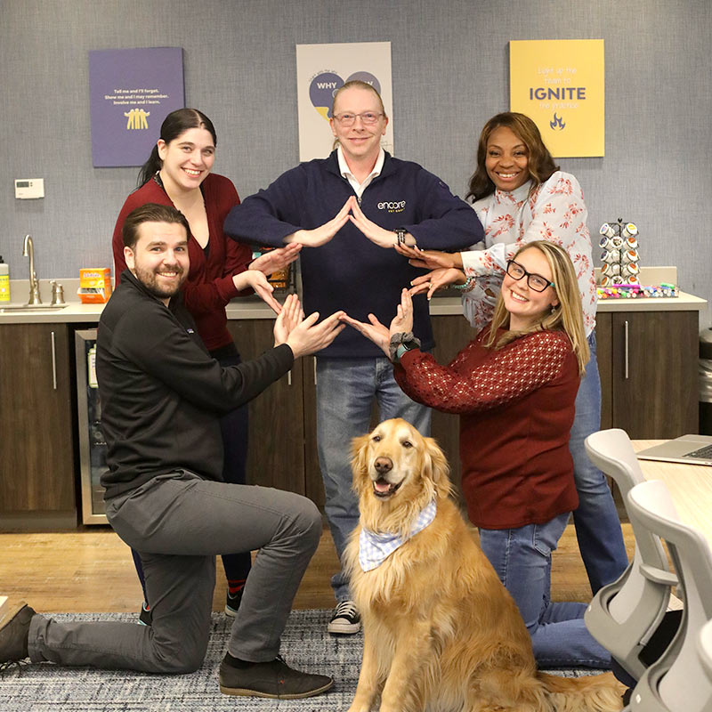 Group of Encore team members gathered together and posing with a golden retriever