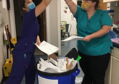 two veterinary staff high fiving each other while using a recycling bin at work