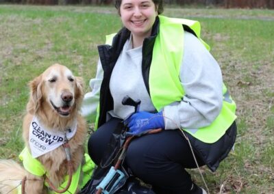 a woman wearing a neon vest smiling at a park with a golden retriever who has his own neon vest