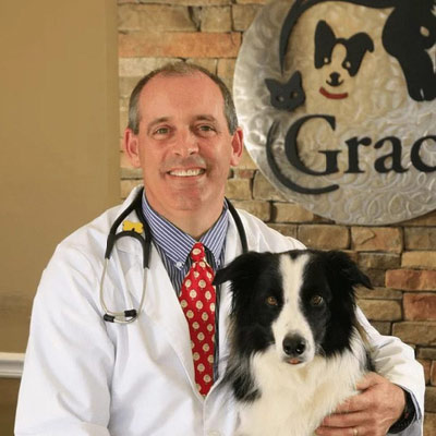 Dr. Tim Loonam standing in front of Grace Animal Hospital sign and holding a black and white dog