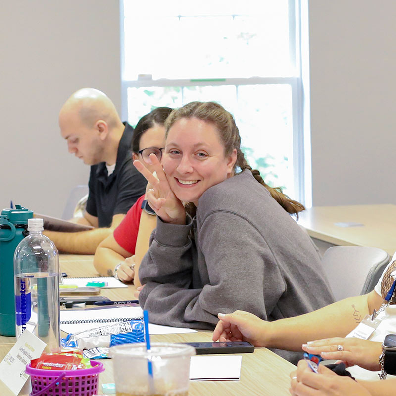 veterinary student smiling and giving a peace sign at a table in a classroom