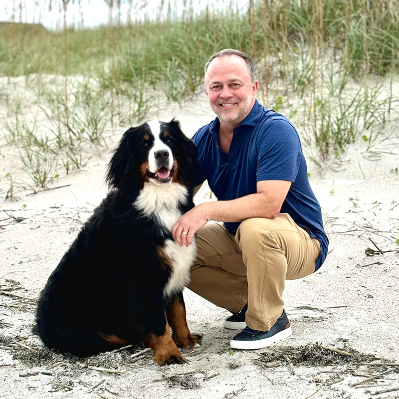 President & CEO Bo Iler with his dog in a grassy beach setting