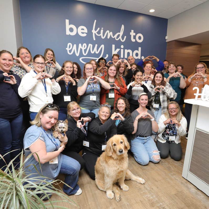 group of Encore team members posing in front of a blue wall that says "Be kind to every kind"