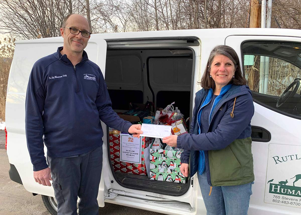 Rutland veterinary team proudly holding up a check in front of a van full of donated items